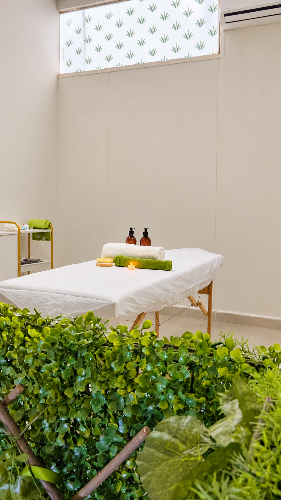 Sala de cuidados da Aloe, com maca preparada, toalhas e vegetação em primeiro plano