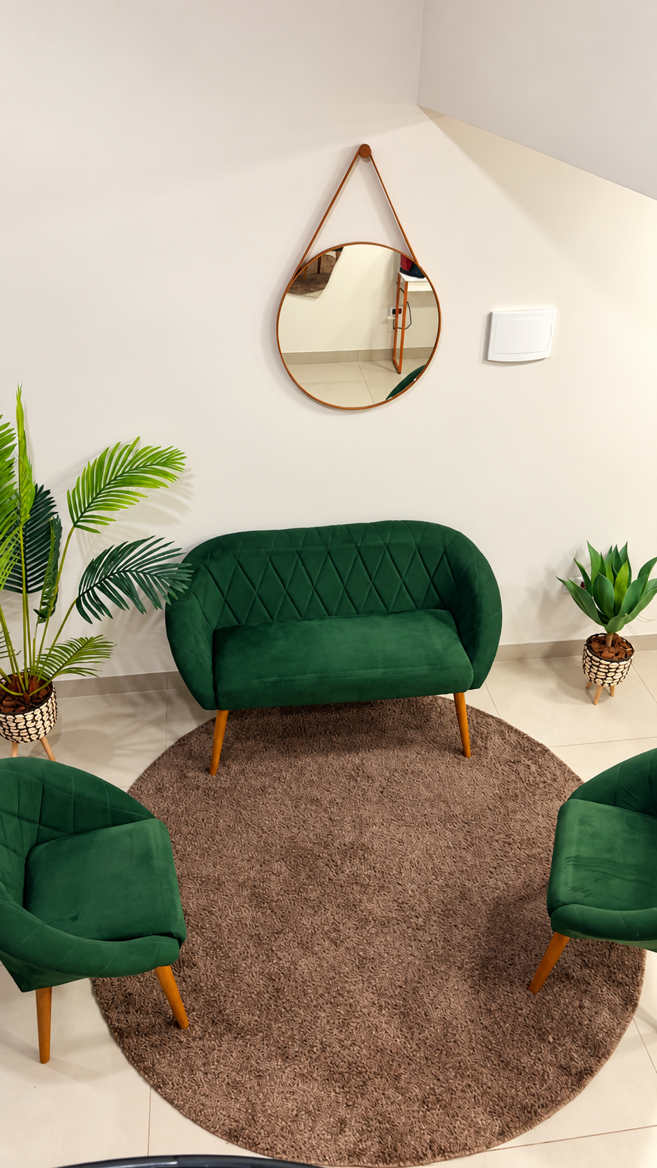 Recepção com sofá e poltronas verdes, espelho redondo e plantas